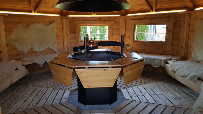 Innenraum der Grillkota am Campingplatz Waldeck mit zentraler Feuerstelle und Holzsitzbank
