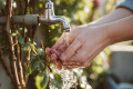 Person wäscht Hände unter einem Außenwasserhahn im Garten